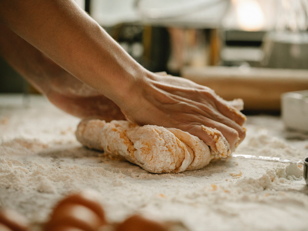 Handen kneden deeg op een met bloem bestoven werkblad in een keuken