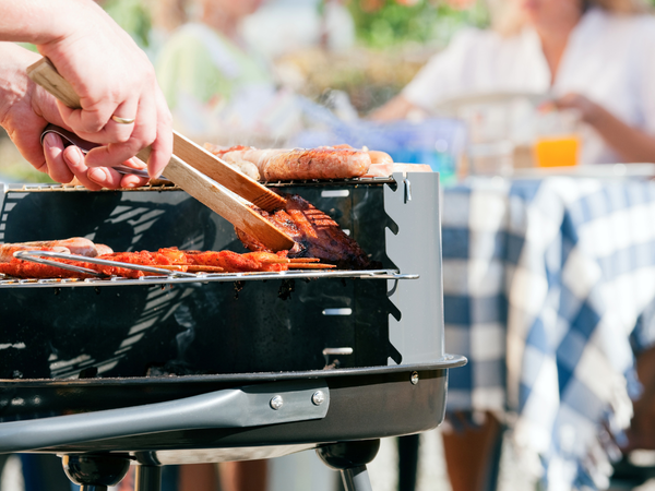 Persoon draait vlees om op een barbecue terwijl gasten op de achtergrond aan tafel zitten