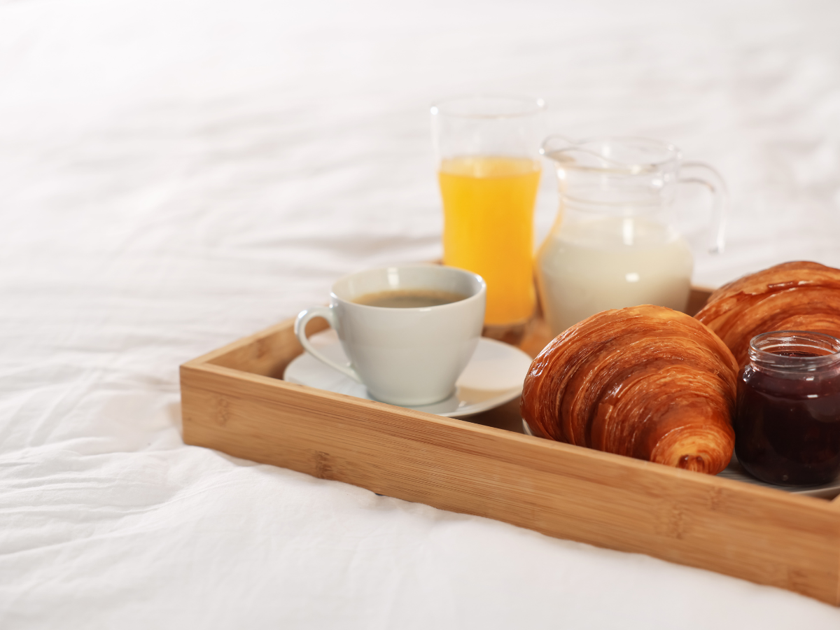 Ontbijt op bed met koffie, croissants, sinaasappelsap, melk en confituur op een houten dienblad