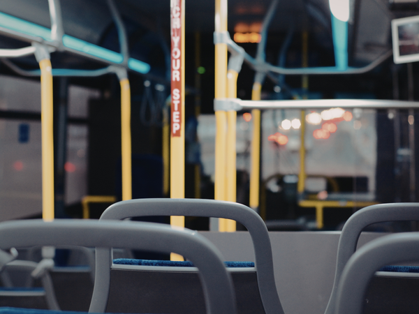 Interieur van een stadsbus met lege zitplaatsen, gele handgrepen en een stopknop op de achtergrond