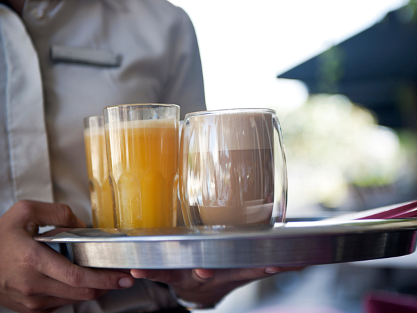 Medewerker serveert drankjes op een dienblad met glazen sinaasappelsap en een warme drank