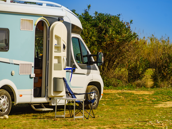 Camper met open deur op een zonnige kampeerplaats, met twee kampeerstoelen naast het voertuig