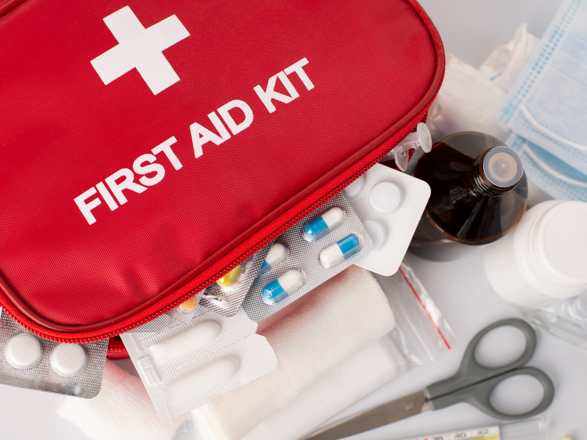 Rode EHBO-kit met verband, medicatie, schaar, flesjes en mondmasker op een witte ondergrond