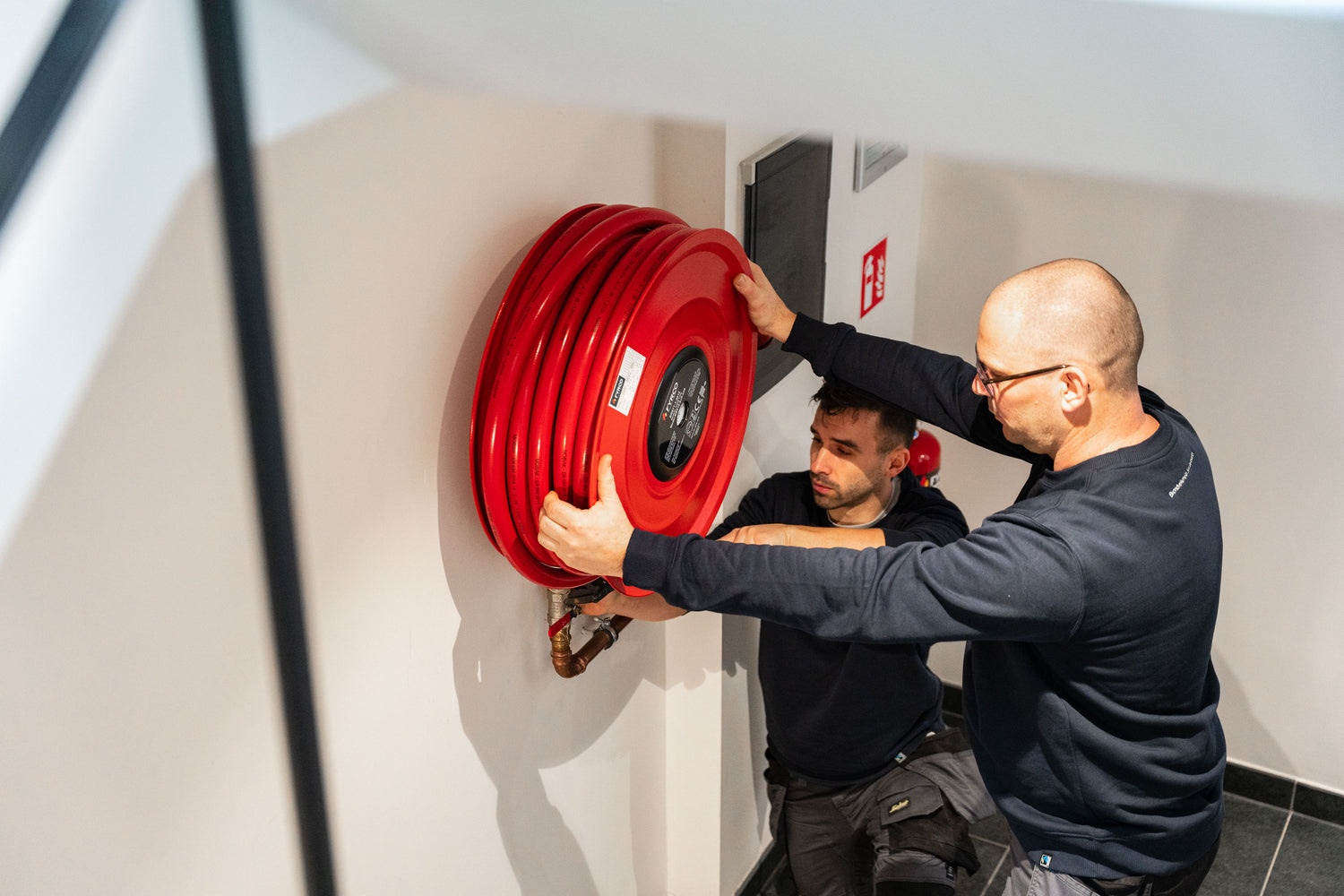 Twee FYRCO-techniekers installeren brandhaspel aan muur