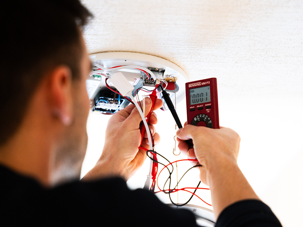 Technieker controleert de spanning van de batterij in een noodverlichtingsarmatuur tijdens onderhoud.