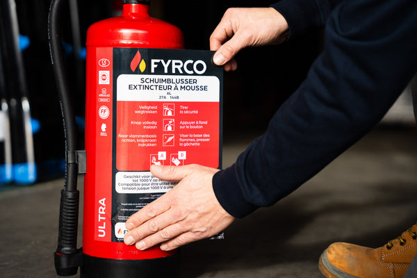 magazijnier plakt FYRCO-label op schuimbrandblusser in magazijn.
