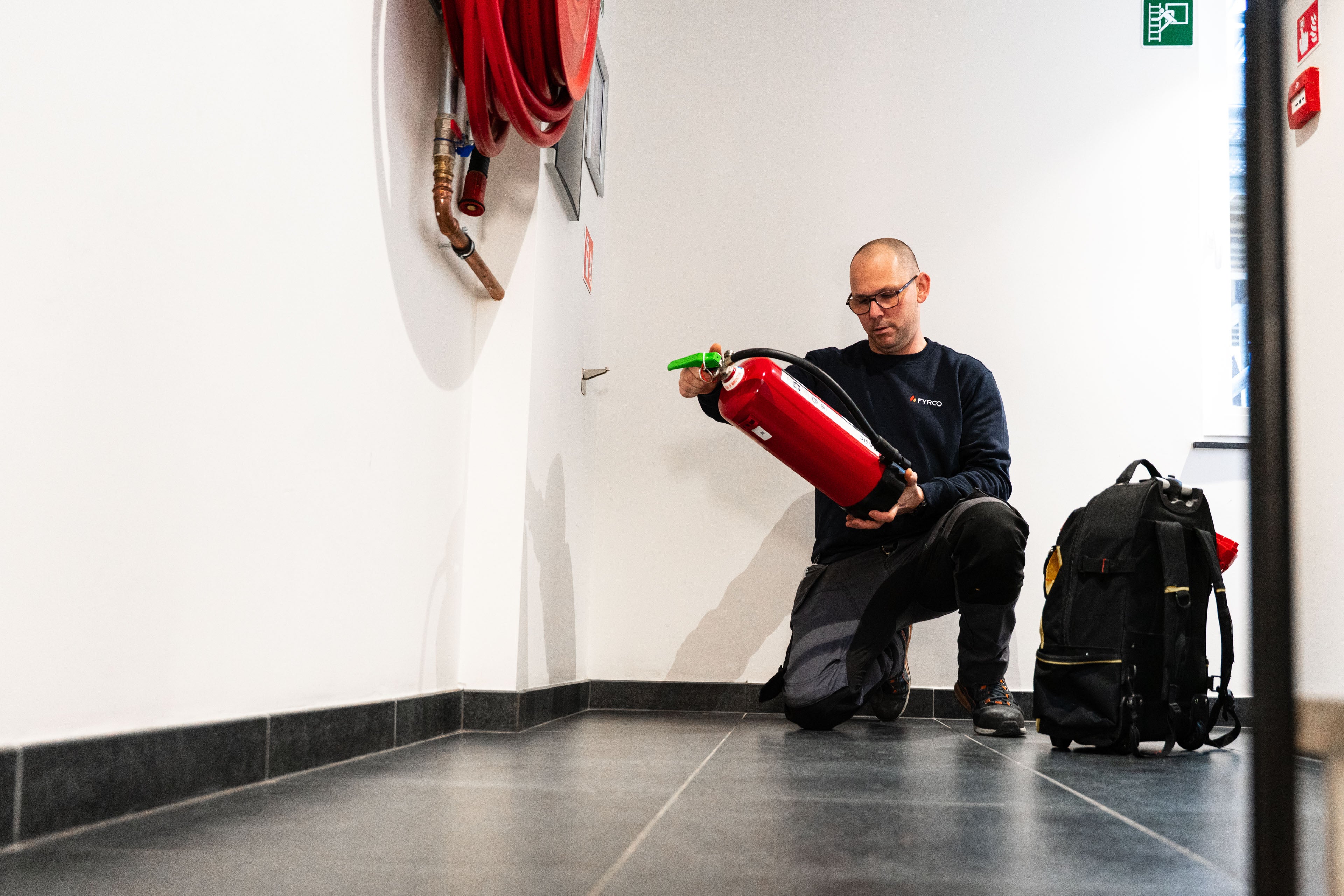 FYRCO-technieker controleert en onderhoudt een brandblusser in een gang bij een klant.