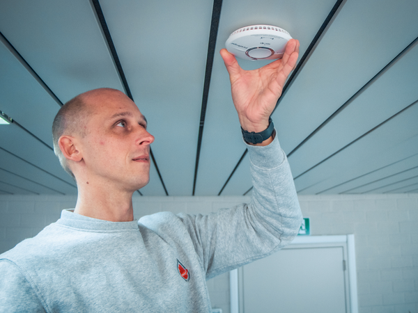Technieker hangt rookmelder op aan plafond in kantoorgebouw