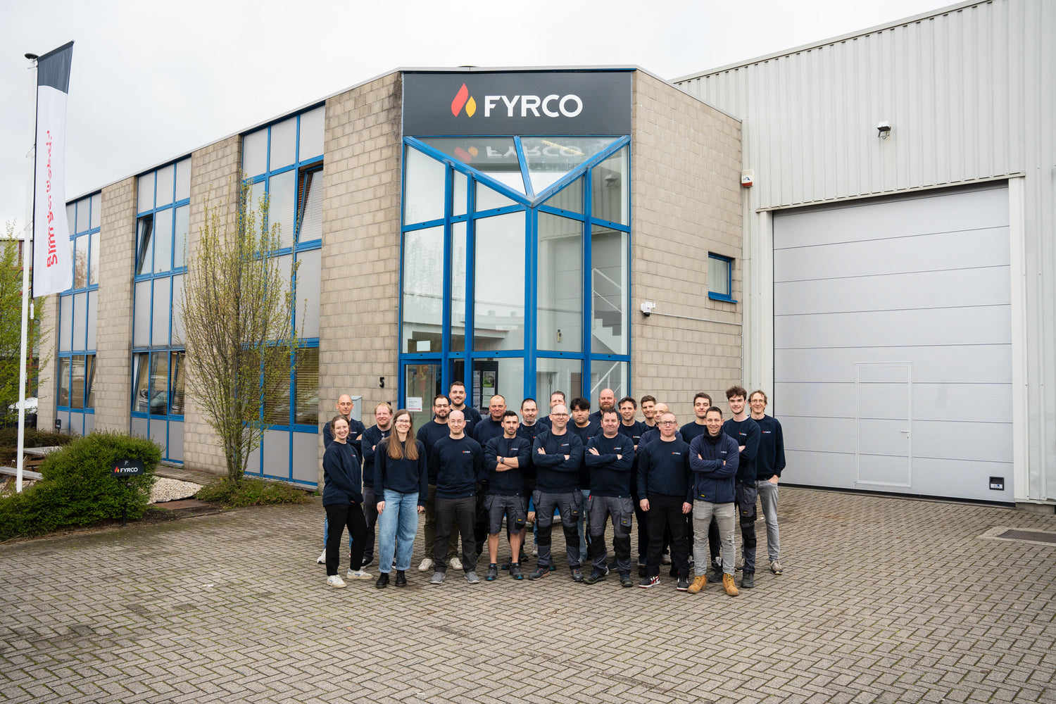 Groepsfoto van het FYRCO-team voor het bedrijfsgebouw, met medewerkers in bedrijfskleding op de binnenplaats