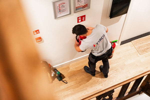 Technieker van FYRCO plaatst een brandblusser in de gang van een studentenkot, met bijhorende signalisatie.